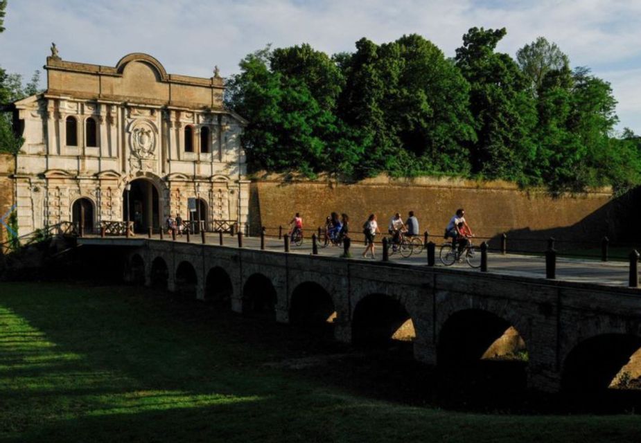 Un gruppo WeRoad attraversa a piedi e in bicicletta un ponte ad arco in pietra che porta a un'antica porta fortificata.