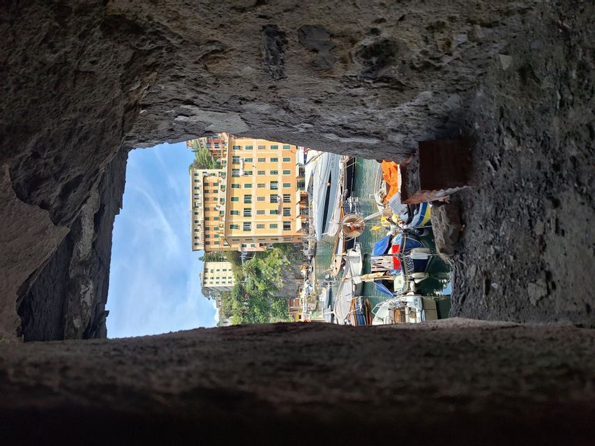 A harbor with colorful buildings and boats is seen through a rectangular opening in a rough stone wall.