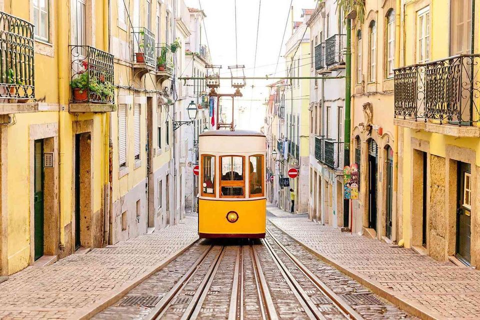 A yellow funicular tram on a track ascends a steep, narrow cobblestone street lined with colorful historic buildings.