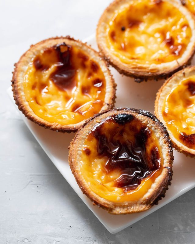 A close-up of several Portuguese custard tarts, pastéis de nata, with caramelized tops on a white rectangular plate.