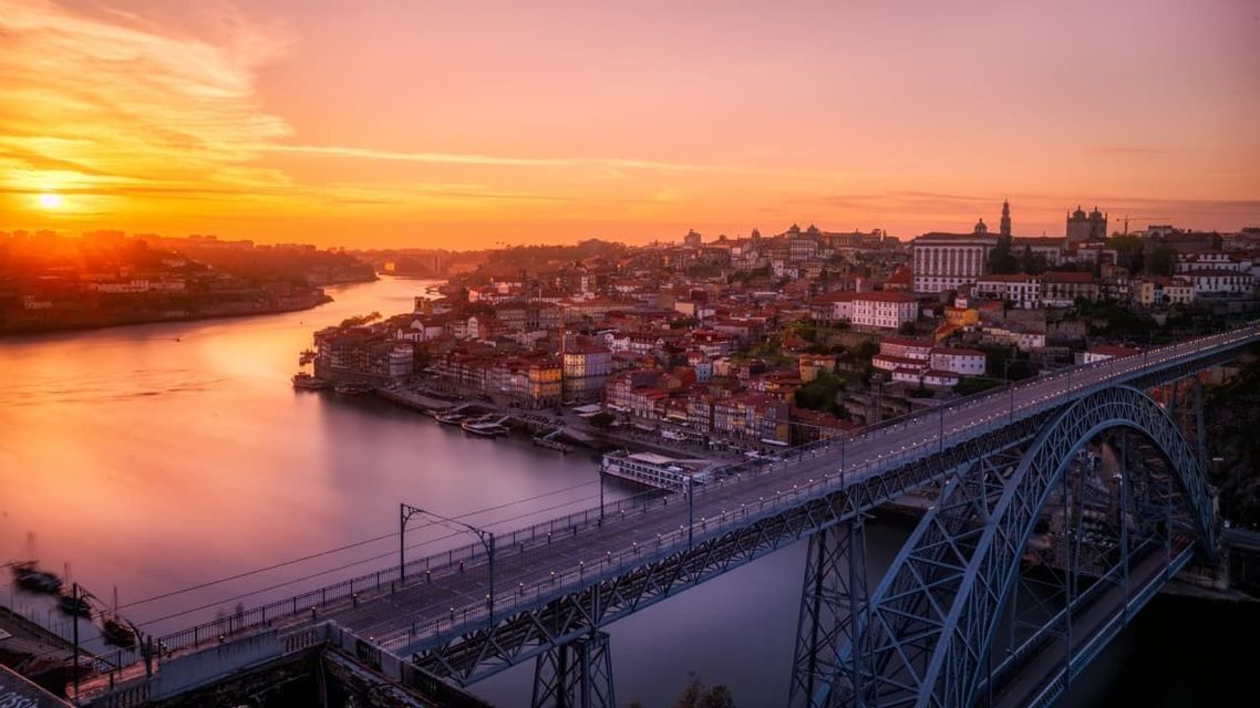 An aerial view of a large metal arch bridge over a river and a cityscape at sunset.