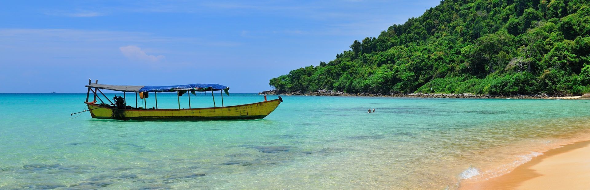 Una barca gialla con un tendalino blu galleggia in acque turchesi cristalline vicino a una spiaggia sabbiosa e a un'isola lussureggiante e alberata.