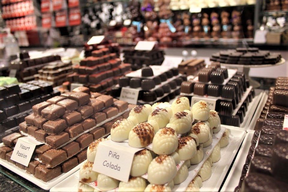 Pyramids of milk, dark, and white chocolates displayed on white trays in a confectionary shop.