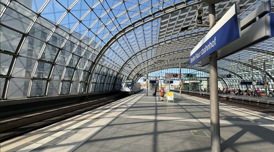 A train waits at a platform in a modern station under a large, arched glass and steel ceiling.