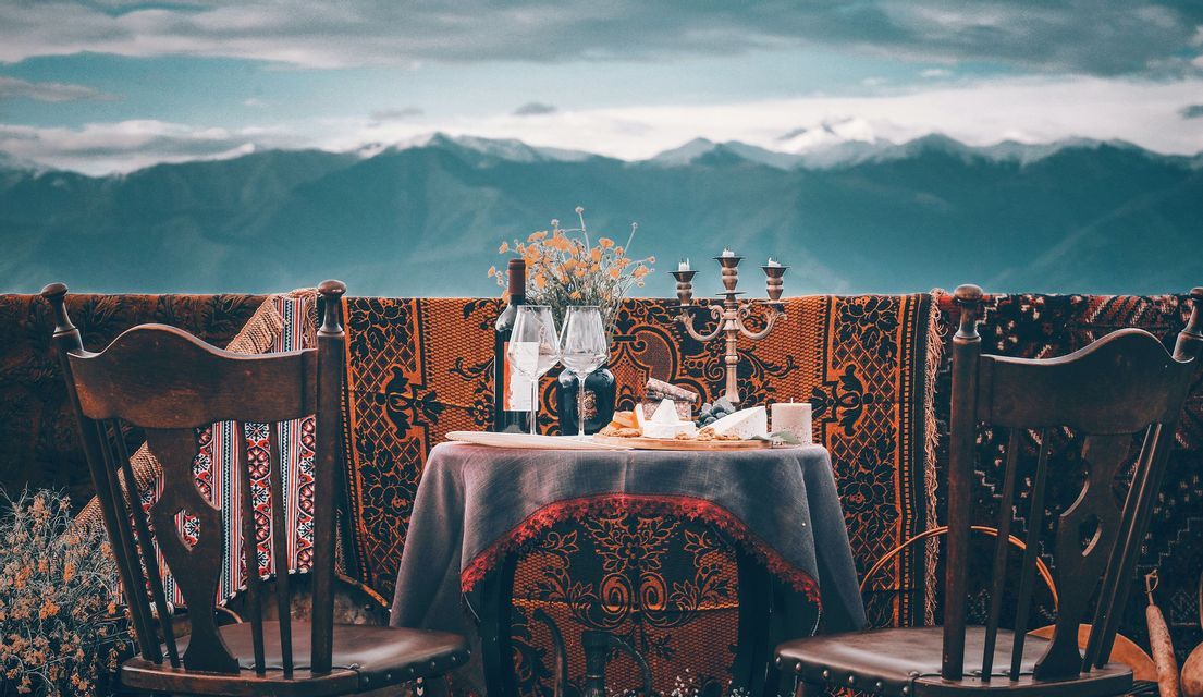 Une table dressée pour deux, avec du vin et du fromage, offrant une vue sur une vaste chaîne de montagnes sous un ciel nuageux.