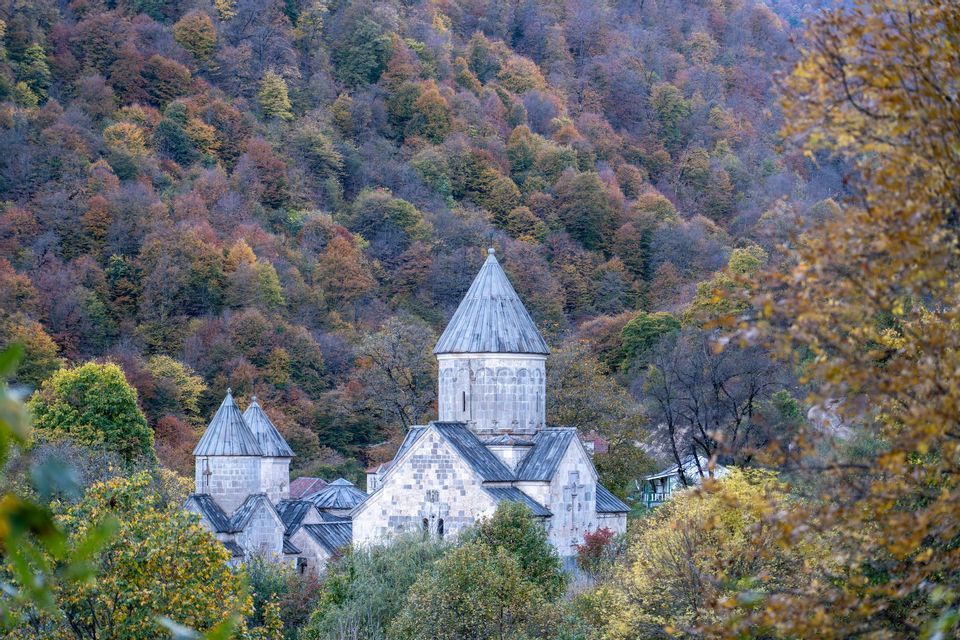 Un monasterio de piedra con chapiteles cónicos está rodeado por un denso bosque en la ladera en pleno color otoñal.