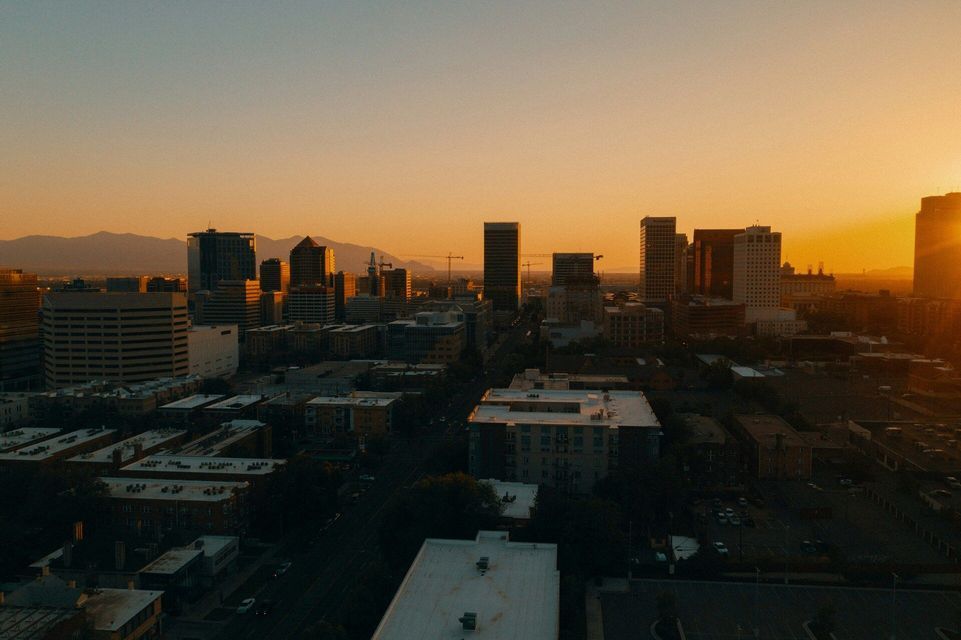 A city skyline with tall buildings and mountains in the background, illuminated by the warm glow of a sunset.