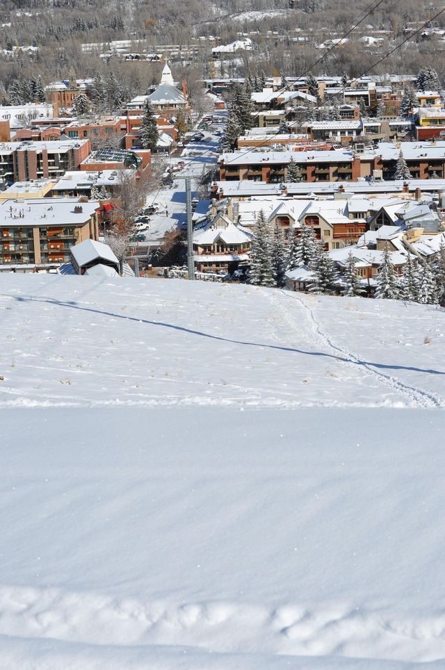 A high-angle view of a snow-covered mountain town from a snowy slope with tracks in the foreground.