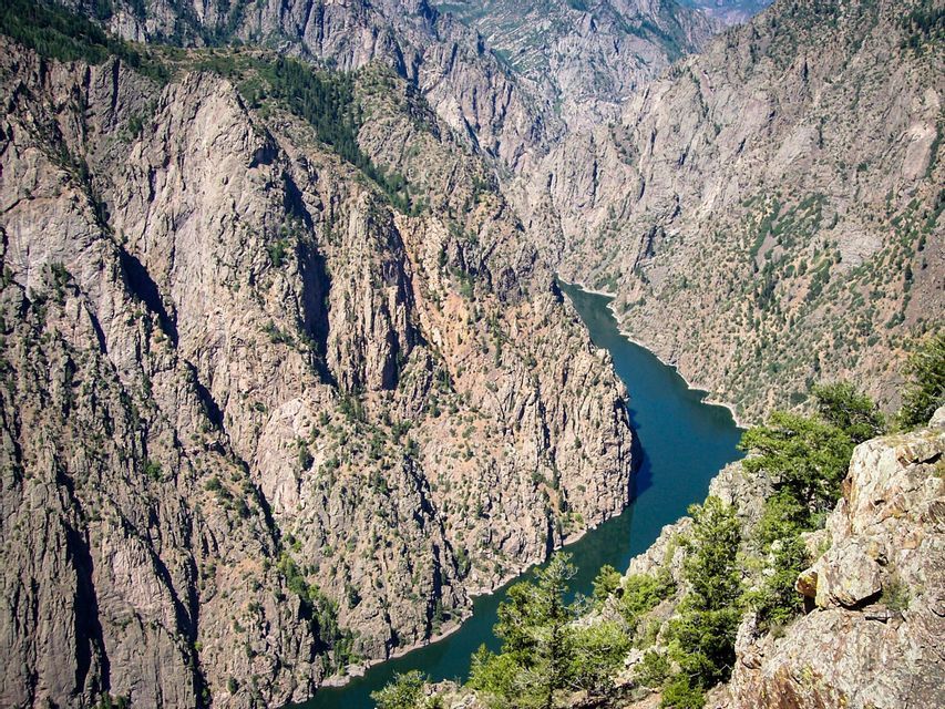 A high-angle view of a deep, rocky canyon with a dark blue river winding through the bottom and sparse green trees on the cliffs.