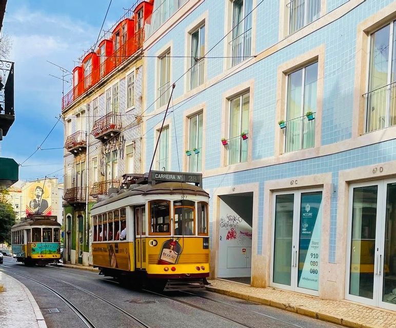 Un classico tram giallo percorre i binari lungo una strada cittadina, accanto a edifici colorati con facciate piastrellate.