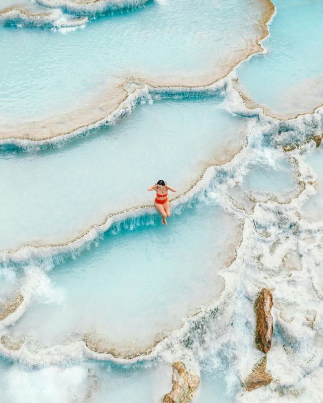 Vista aerea di una donna in bikini rosso che si rilassa in una serie di piscine termali terrazzate azzurre lattiginose.