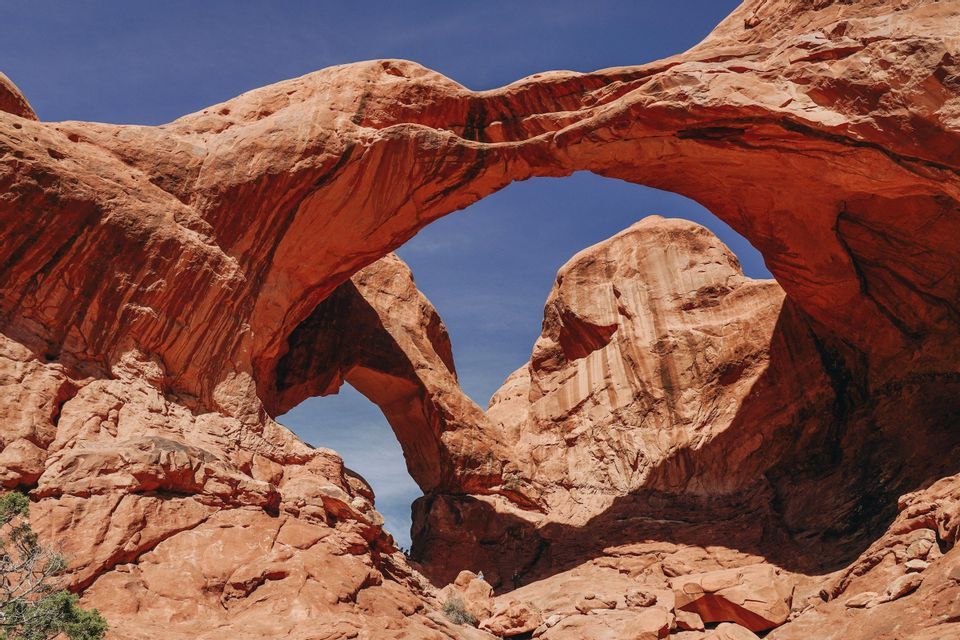Two large, overlapping red rock arches form a double arch against a cloudless blue sky.