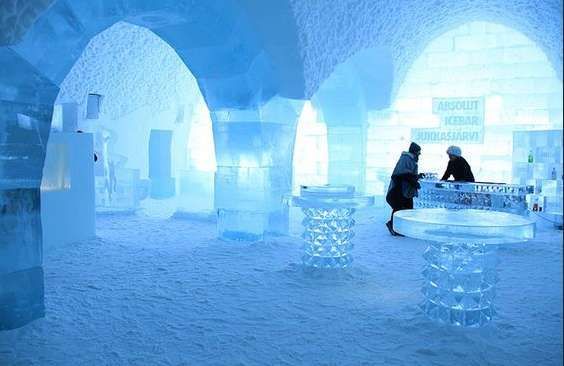 L'intérieur d'un bar entièrement de glace, avec deux personnes en vestes d'hiver se tenant au comptoir de glace, près de tables et d'arches.