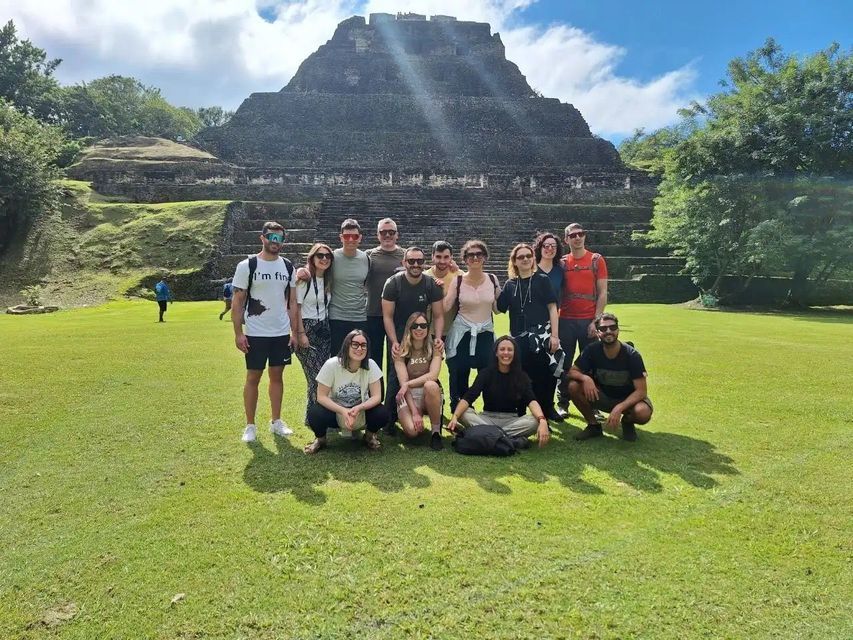 A WeRoad group trip poses for a photo on a grassy lawn with a large, ancient stone pyramid in the background.
