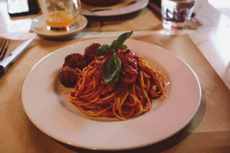A plate of spaghetti and meatballs with tomato sauce, garnished with a basil leaf, on a restaurant table.