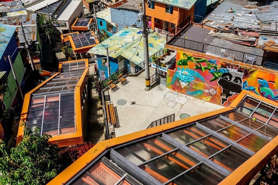 An overhead view of outdoor escalators with orange roofs running through a colorful neighborhood with graffiti on a wall.