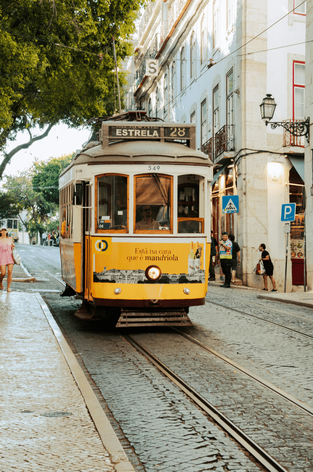 Un tram d'epoca giallo e bianco percorre i binari su una stretta strada di ciottoli accanto a vecchi edifici cittadini.