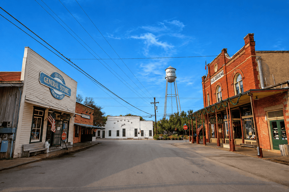 An empty street in a historic town features old-fashioned storefronts and a tall water tower under a clear blue sky.