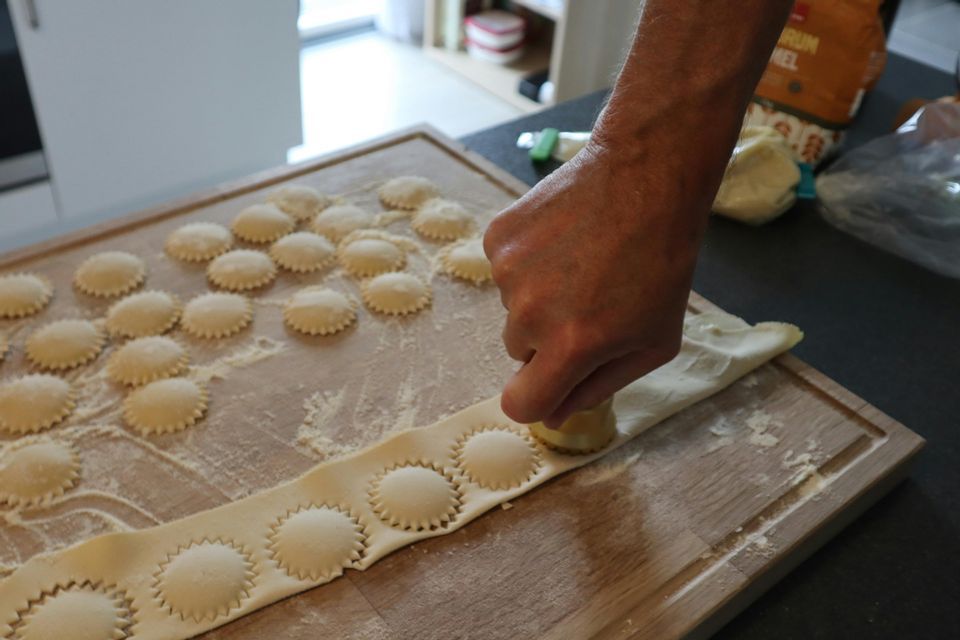A person's hand using a cutter to make fresh ravioli on a wooden board dusted with flour.