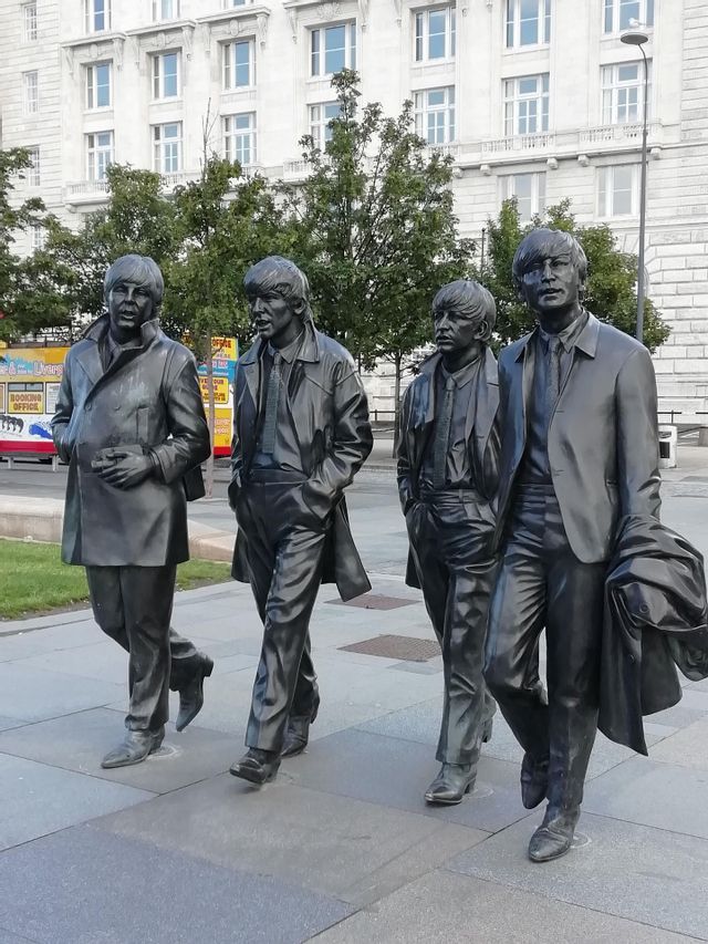 Life-size bronze statues of the four members of The Beatles walking along a city pavement in front of a building.