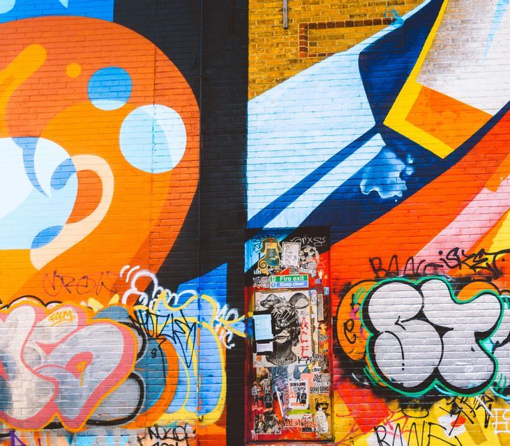 A brick wall covered in vibrant and colorful graffiti, with a door in the center that is plastered with stickers.