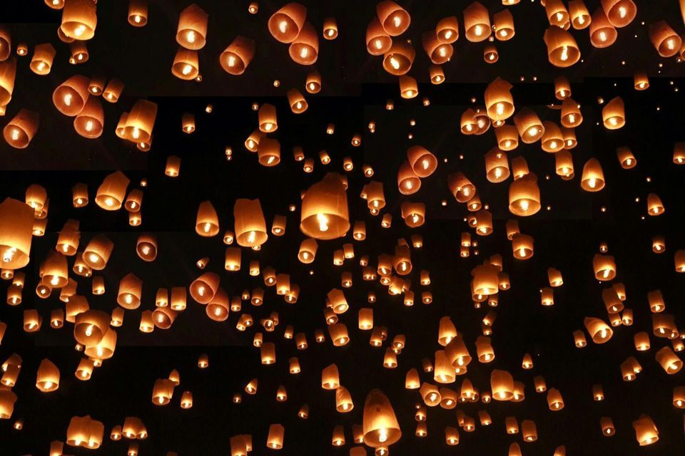 Centinaia di lanterne di carta illuminate fluttuano nel cielo notturno, brillando caldamente.