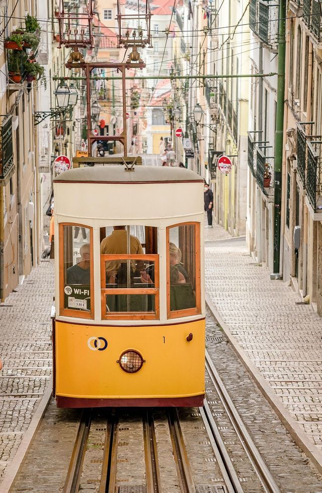 Una funicolare gialla con passeggeri a bordo sale lungo una ripida e stretta strada di ciottoli fiancheggiata da edifici.