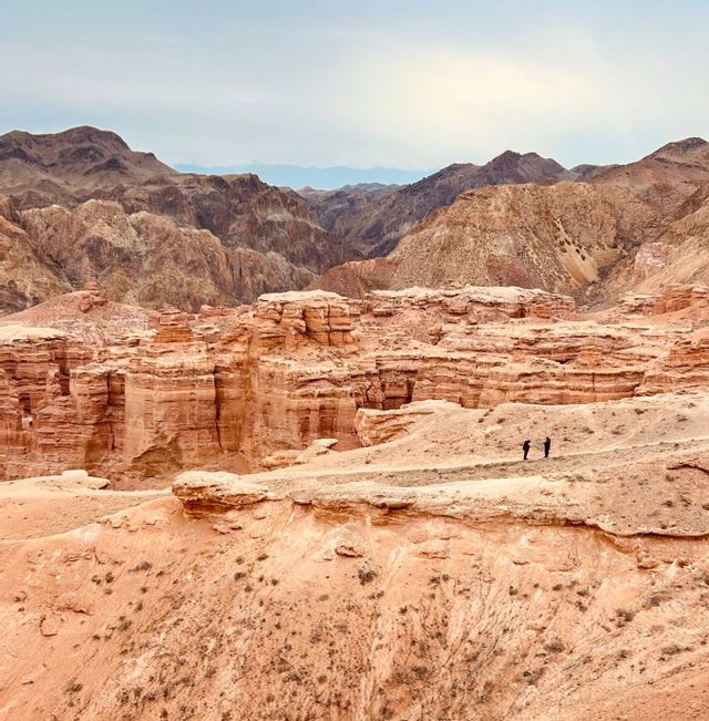 Zwei Personen einer WeRoad-Gruppenreise stehen auf einem Bergrücken und blicken auf einen weiten Canyon aus roten Felsformationen.