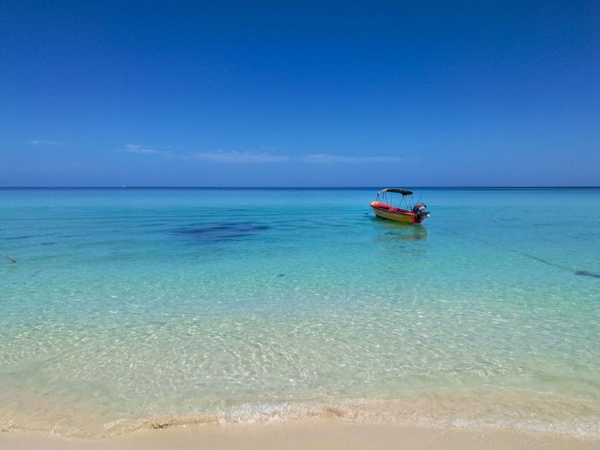 A yellow motorboat anchored in calm, turquoise ocean water near a sandy beach under a clear blue sky.