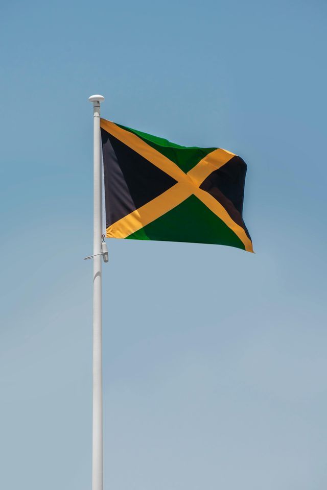 The Jamaican flag waving on a white flagpole against a clear blue sky.