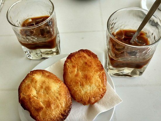 Due bicchieri di caffè freddo e due pasticcini rotondi su un piatto posati su un tavolo bianco.