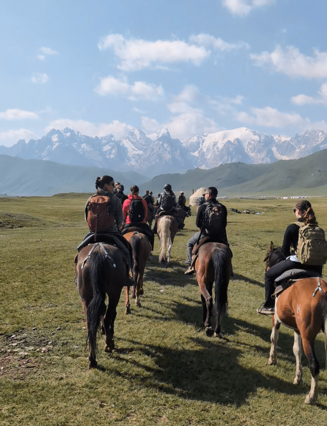 Eine WeRoad Gruppenreise zu Pferd über eine Graslandschaft auf schneebedeckte Berge zu.