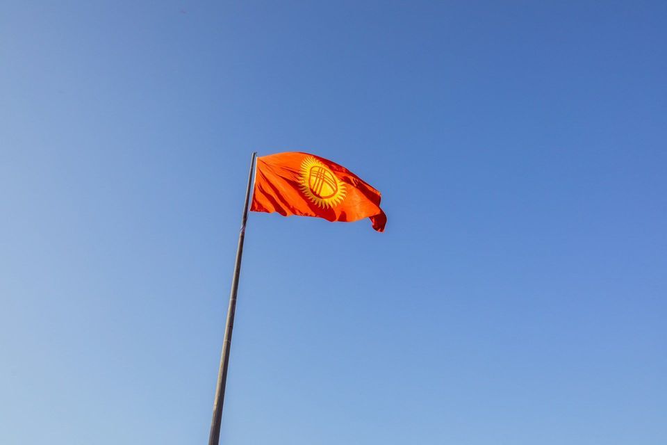 Die rot-gelbe Flagge Kirgisistans weht an einem hohen Fahnenmast vor einem klaren blauen Himmel.