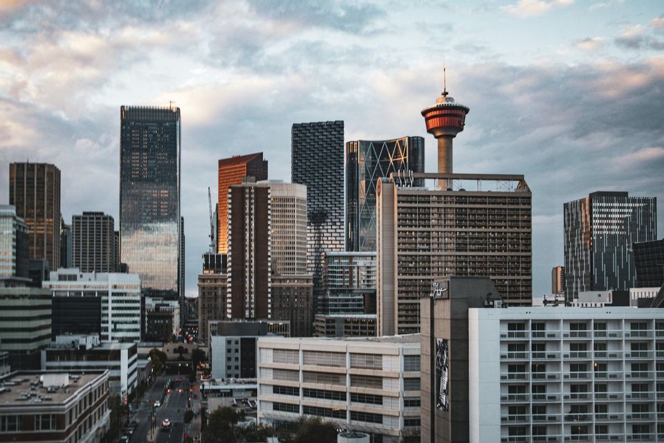 A dense city skyline with numerous skyscrapers and an observation tower under a cloudy sky during sunset.