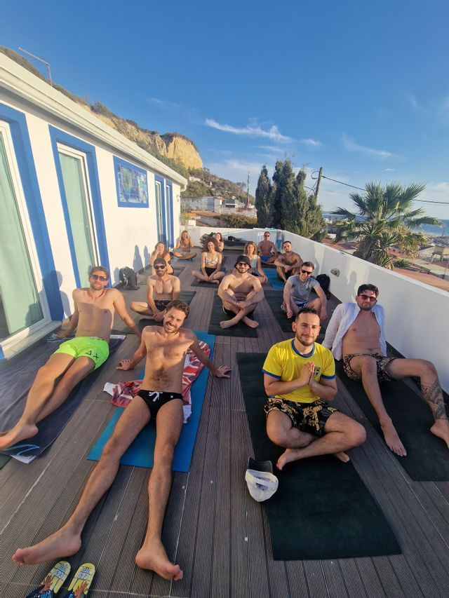 Un gruppo WeRoad è seduto su tappetini da yoga su una terrazza soleggiata sul tetto, in posa per una foto dopo una sessione di yoga.