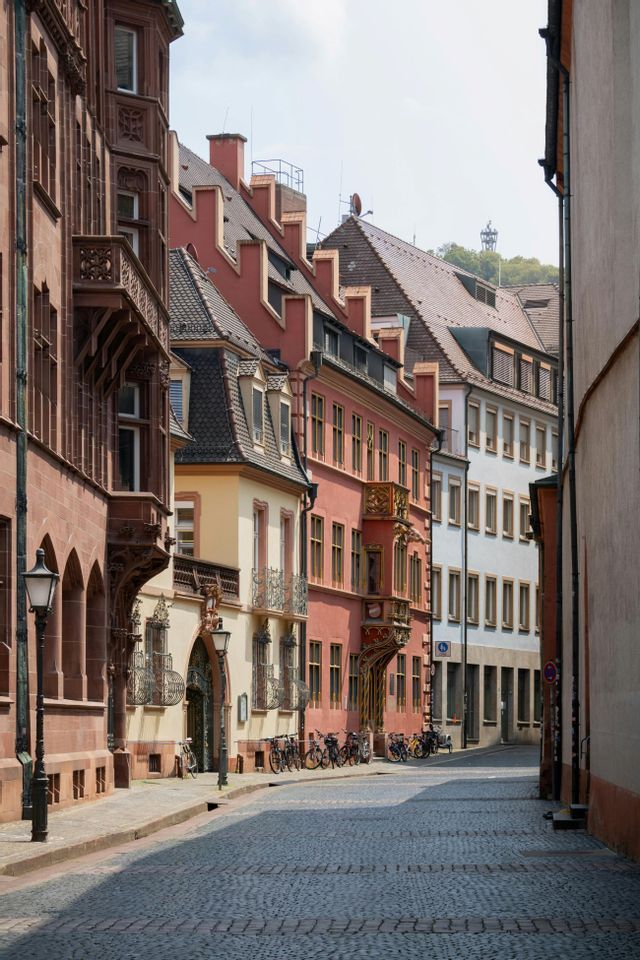 Una stretta strada acciottolata, fiancheggiata da edifici storici e colorati, con biciclette parcheggiate in una giornata di sole.