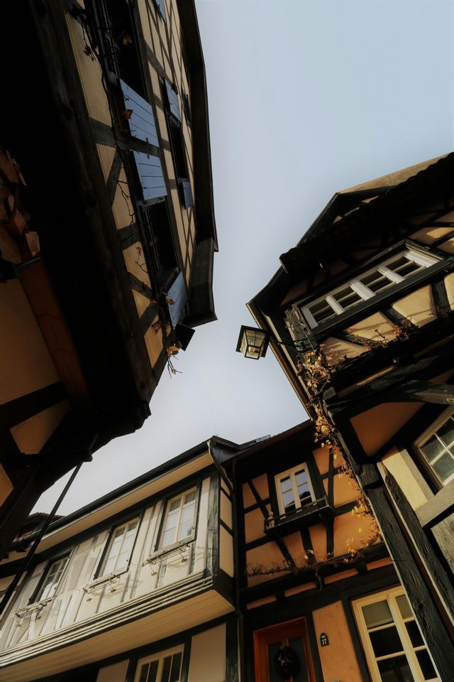 Una vista dal basso di tradizionali edifici a graticcio che fiancheggiano una strada stretta sotto un cielo pallido.