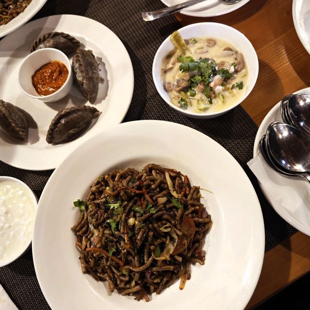 Eine Draufsicht auf verschiedene asiatische Gerichte auf einem Tisch, darunter Nudeln, Teigtaschen mit Dip-Sauce und eine cremige Suppe.