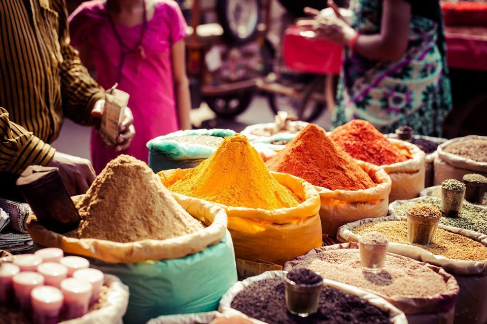 Colorful mounds of yellow, red, and brown powdered spices are displayed in large open sacks at a bustling outdoor market.