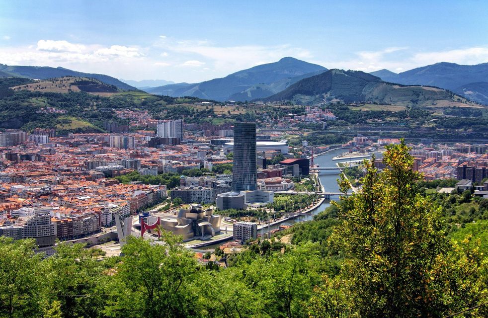 A panoramic view of a city with a winding river, nestled in a valley with green hills and distant mountains.