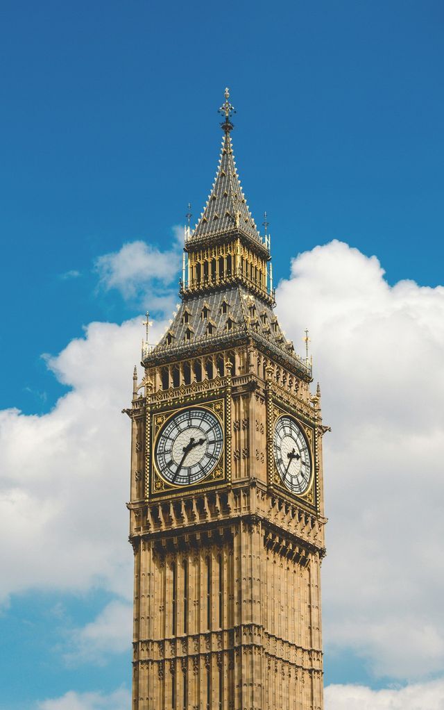 A low-angle shot of the Big Ben clock tower against a blue sky with white clouds.