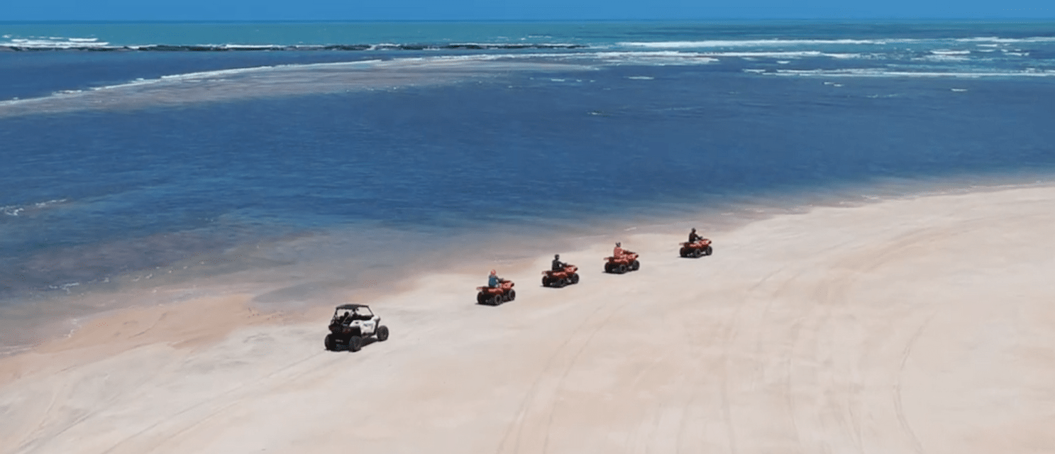 Un gruppo WeRoad guida quad e UTV in fila lungo una spiaggia sabbiosa accanto all'oceano blu.