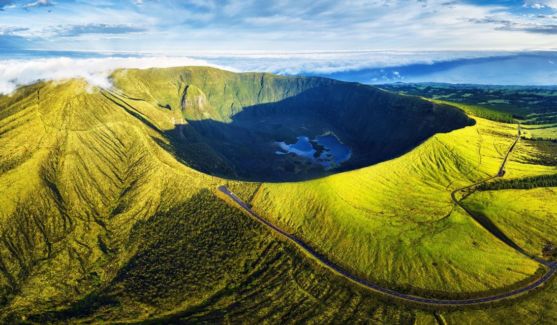 Una vista aerea di un grande cratere vulcanico verde con un lago sul fondo e una strada che si snoda lungo il suo bordo.