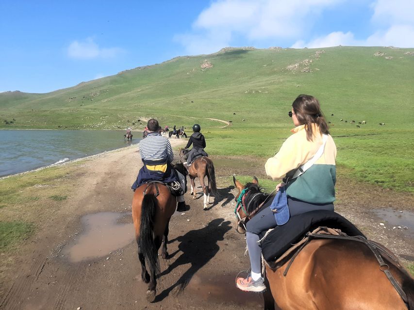 Un voyage de groupe WeRoad à cheval sur un chemin de terre le long d'un lac, avec des collines verdoyantes en arrière-plan.