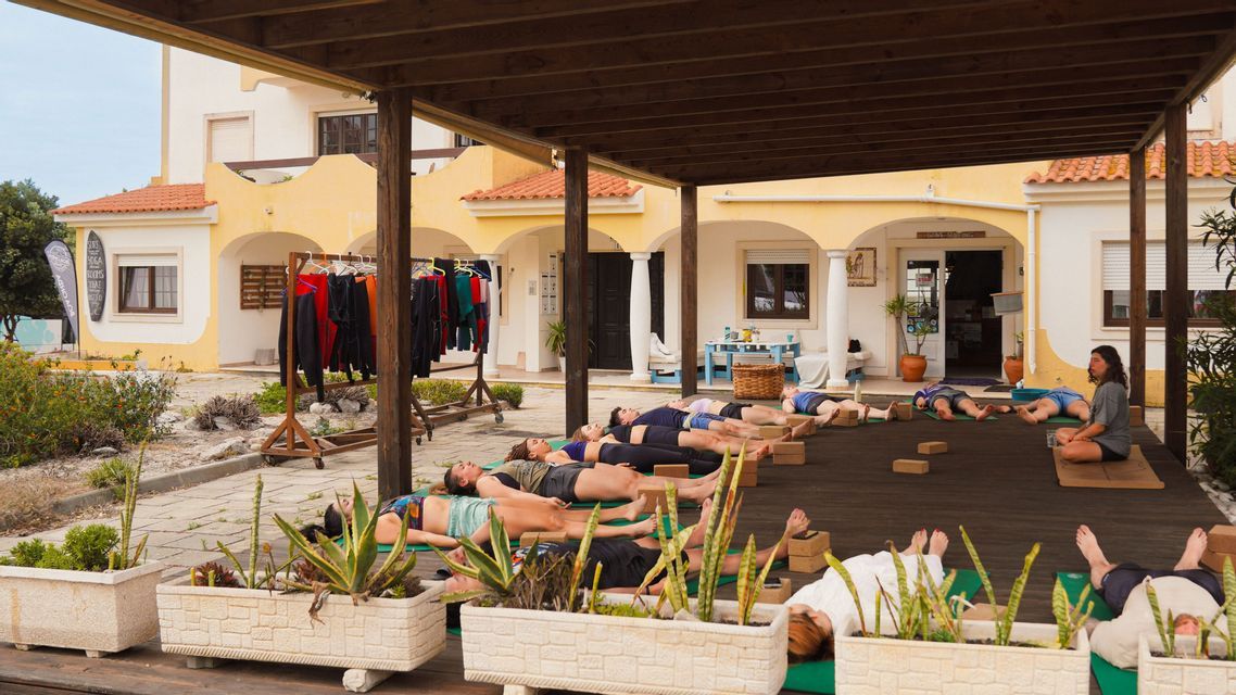Un viaggio di gruppo WeRoad pratica yoga, sdraiato in posa di rilassamento su tappetini su una piattaforma esterna coperta.