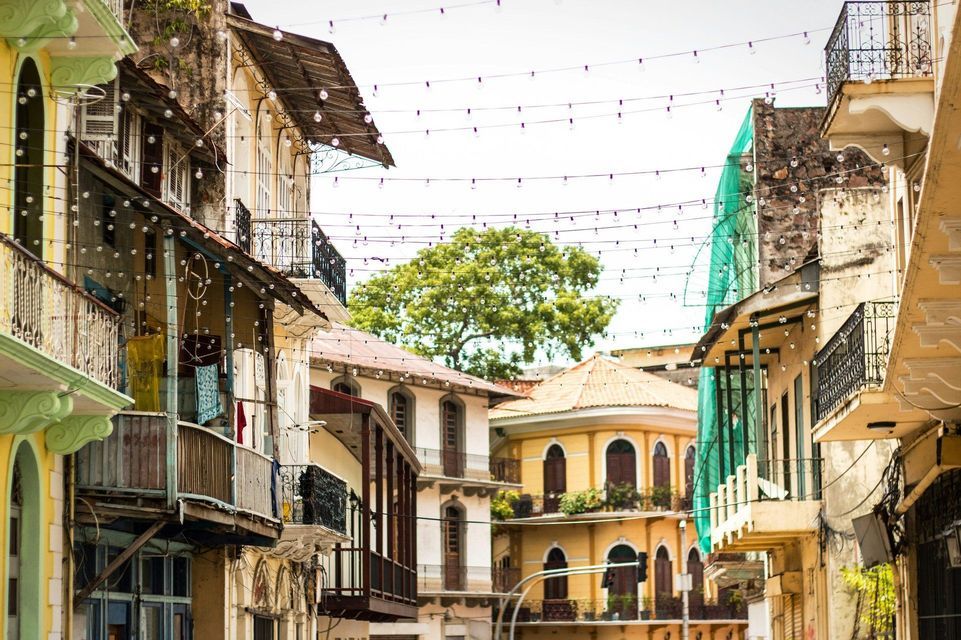 A narrow street is lined with colorful colonial-style buildings featuring balconies and strings of lights crisscrossing overhead.
