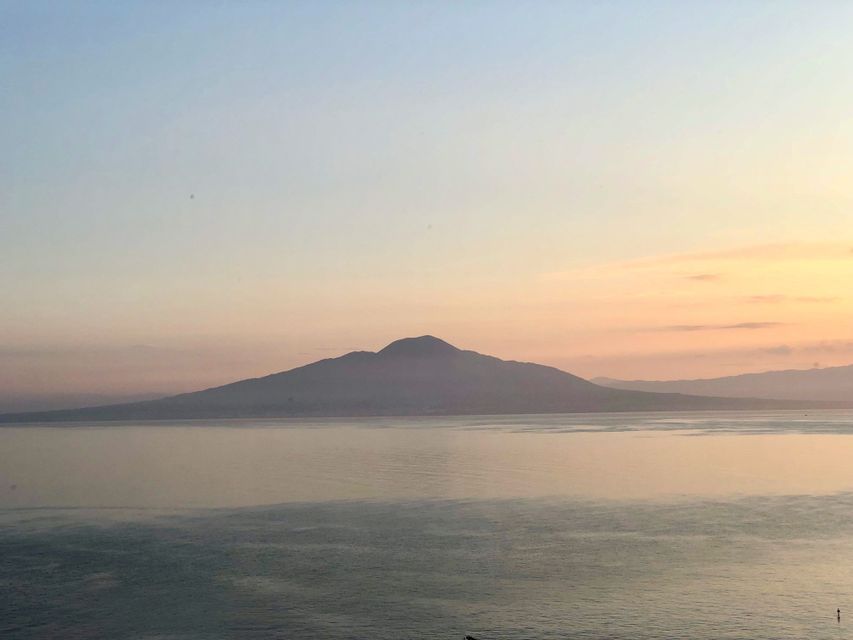 Une grande montagne se découpe en silhouette sur un ciel de coucher de soleil pastel au-dessus d'un plan d'eau calme.