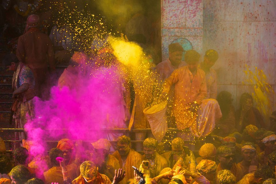 Una folla di persone a un festival lancia polvere gialla e rosa vibrante in aria.