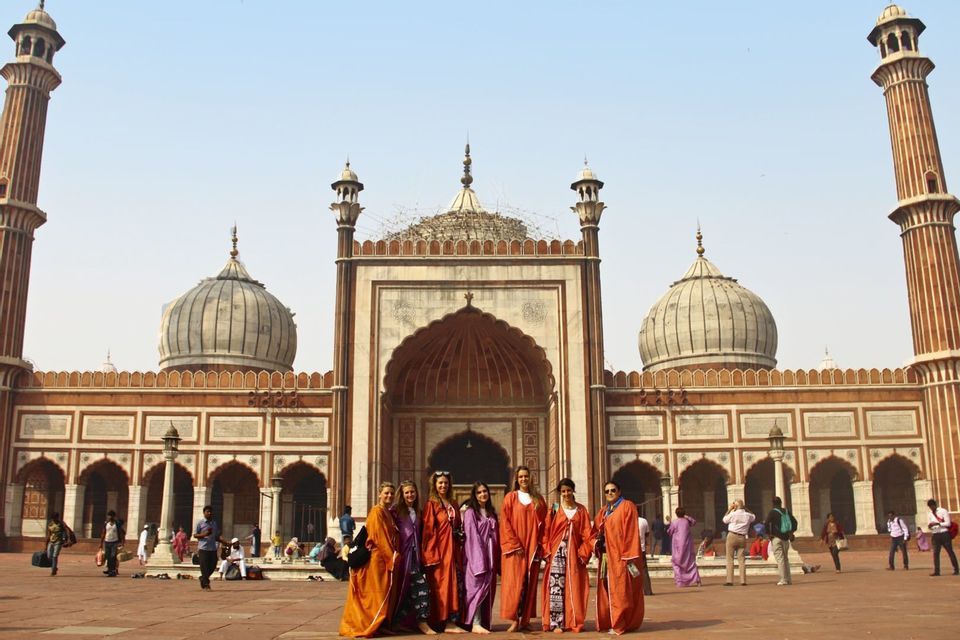 A WeRoad group trip of women wearing colorful robes pose for a photo in front of an ornate mosque with large domes.