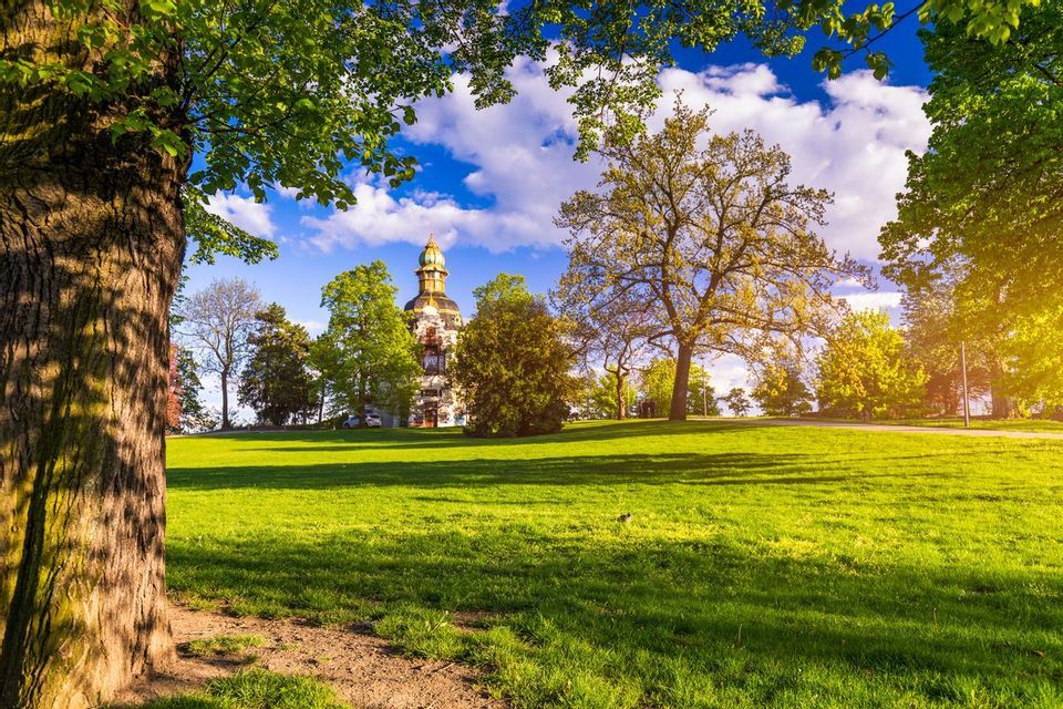 Un bâtiment historique avec un dôme sur une colline herbeuse, entouré d'arbres verts sous un ciel partiellement nuageux.